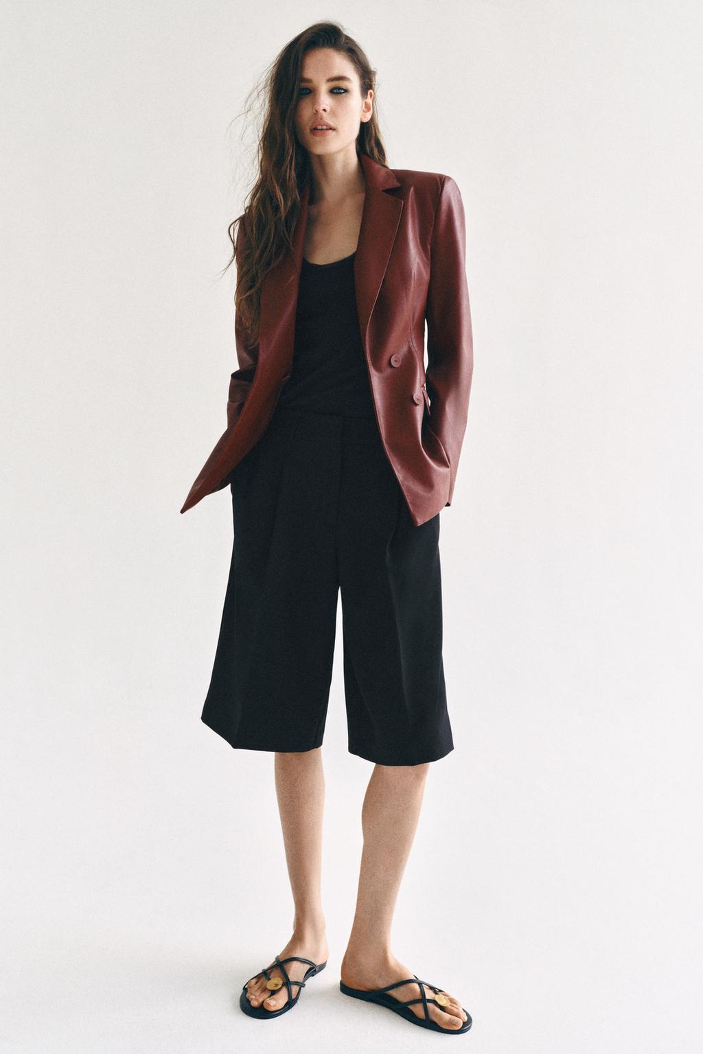 Woman wearing a burgundy leather blazer with black tailored bermuda shorts, styled for smart/office wear