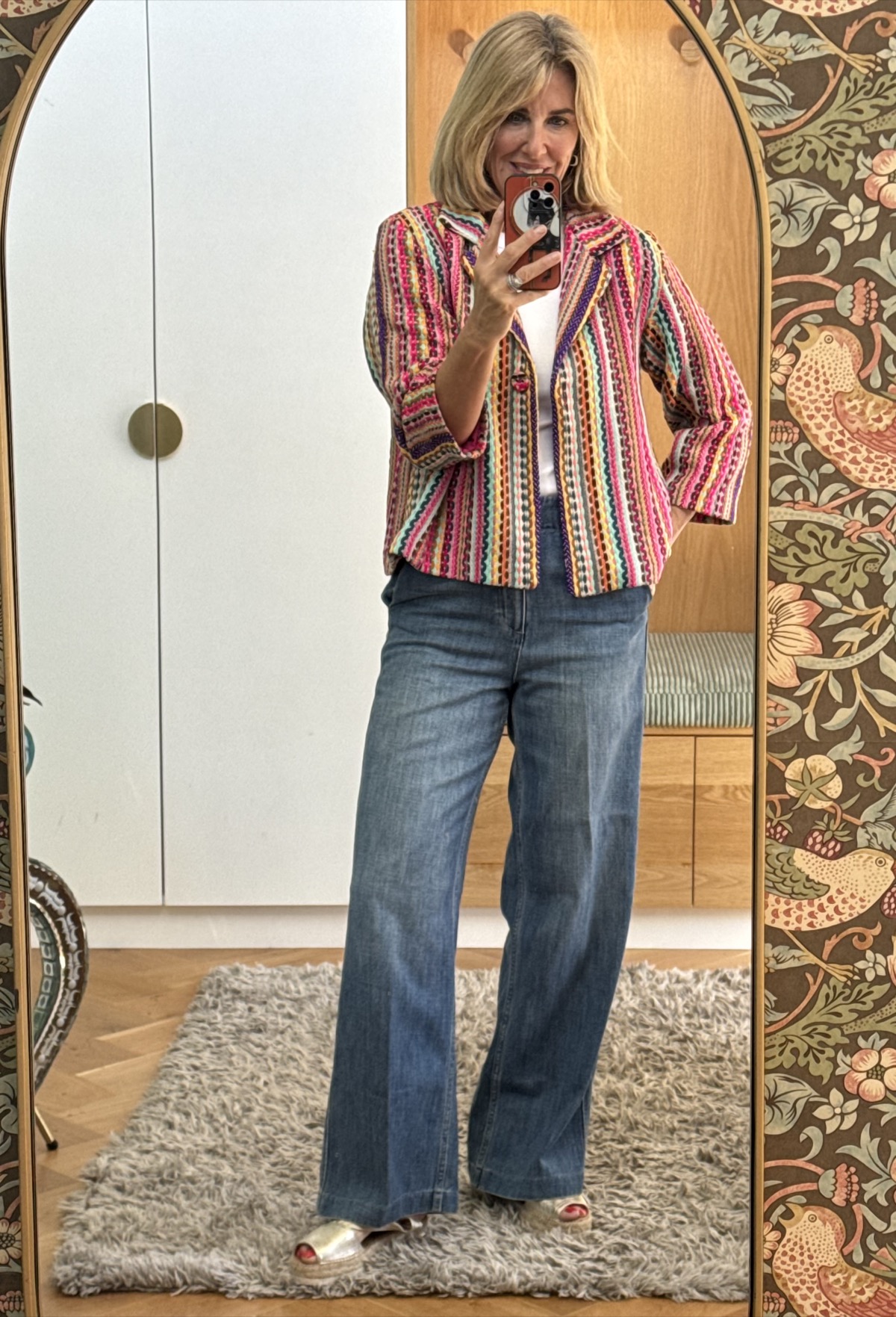 Julie wearing the Delphine jacket in a bold pink, red and multicolour stripe weave, same white top and blue jeans styling