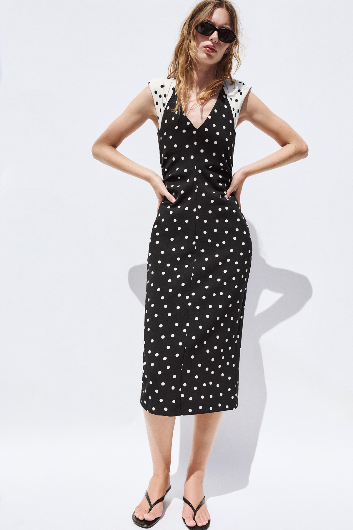 Woman in a black and white polka dot midi dress with structured shoulder pads and a V-neck