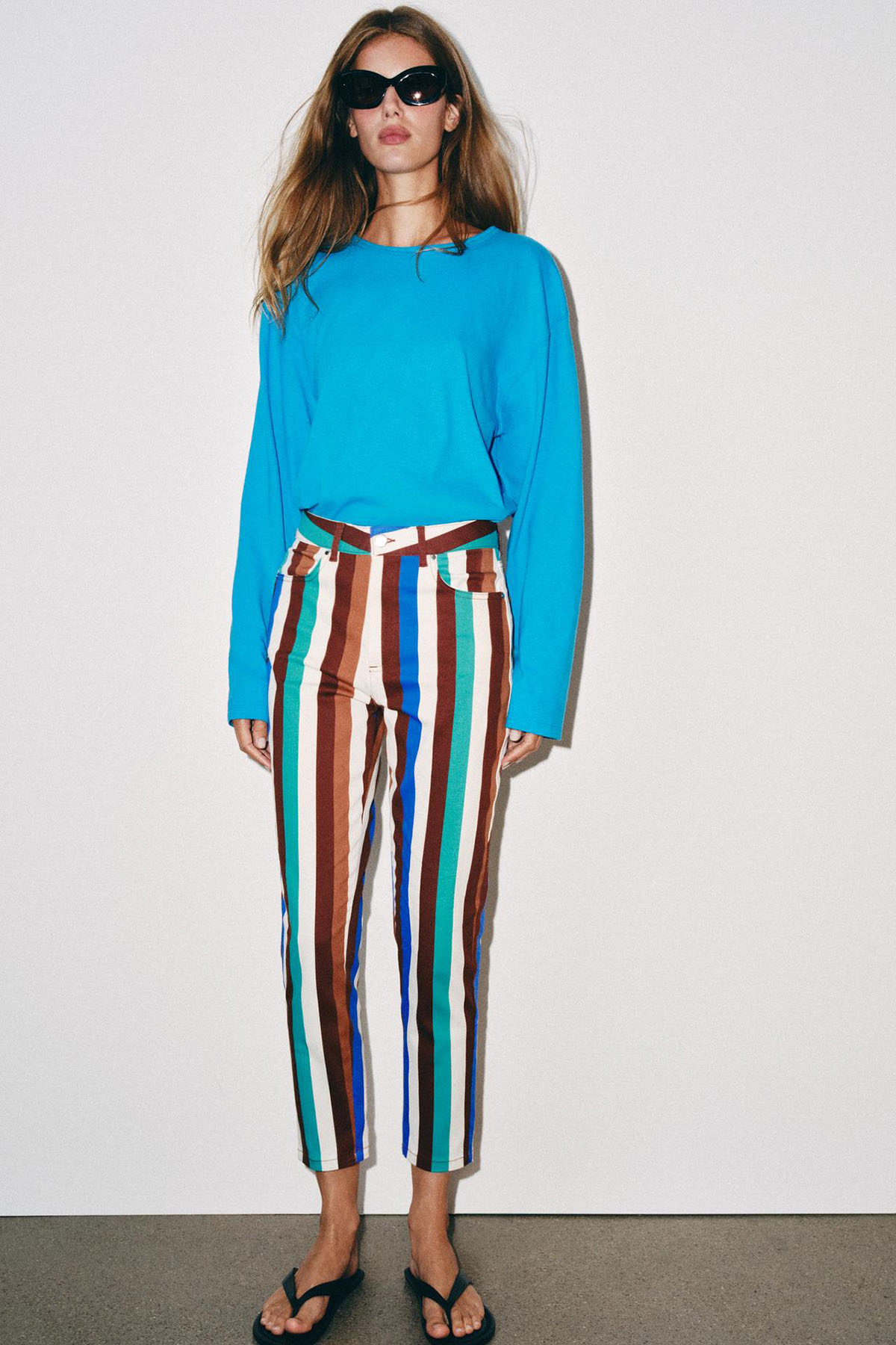 Woman wearing multi-coloured striped mom-fit trousers in brown, teal, blue and cream, with a bright blue top