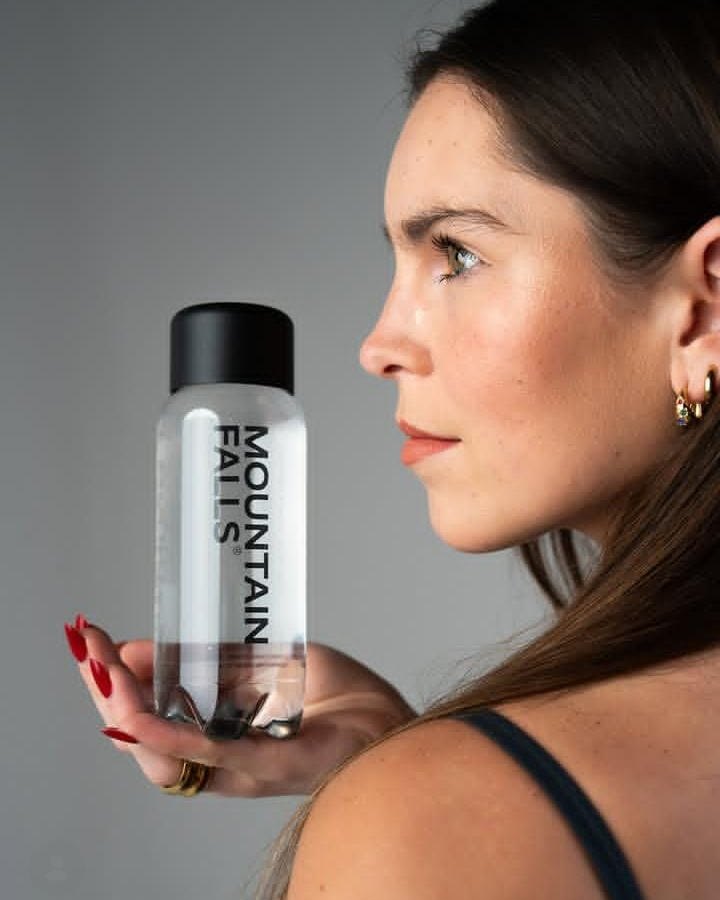 A woman in profile holding up a clear bottle of Mountain Falls still mineral water