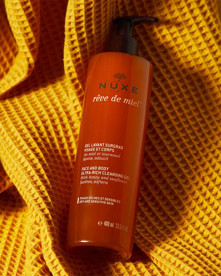 A bottle of Nuxe Rêve de Miel face and body cleansing gel resting on a golden waffle-weave towel